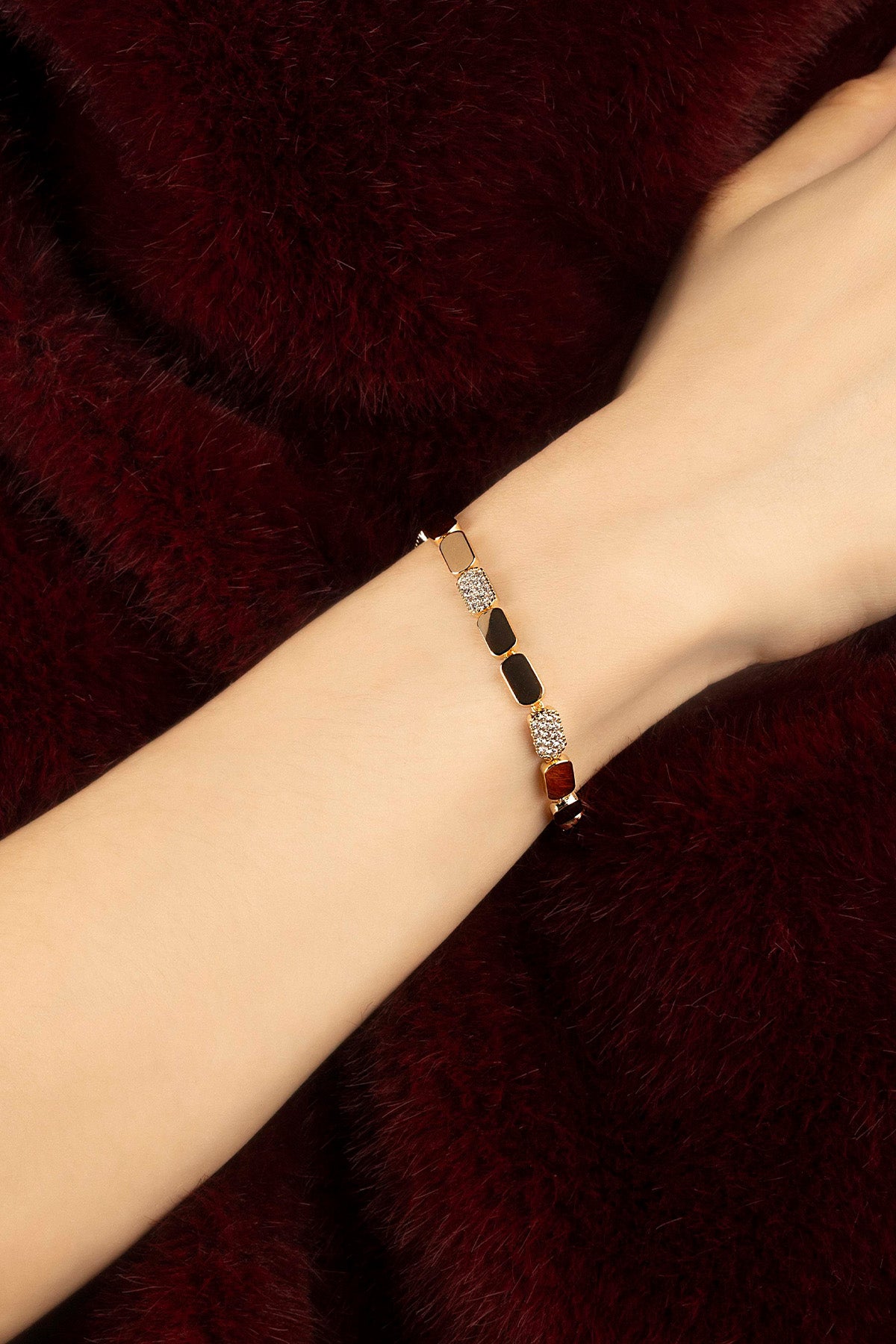 Woman wearing APM bracelet, a golden rhythm of colors against burgundy warmth.