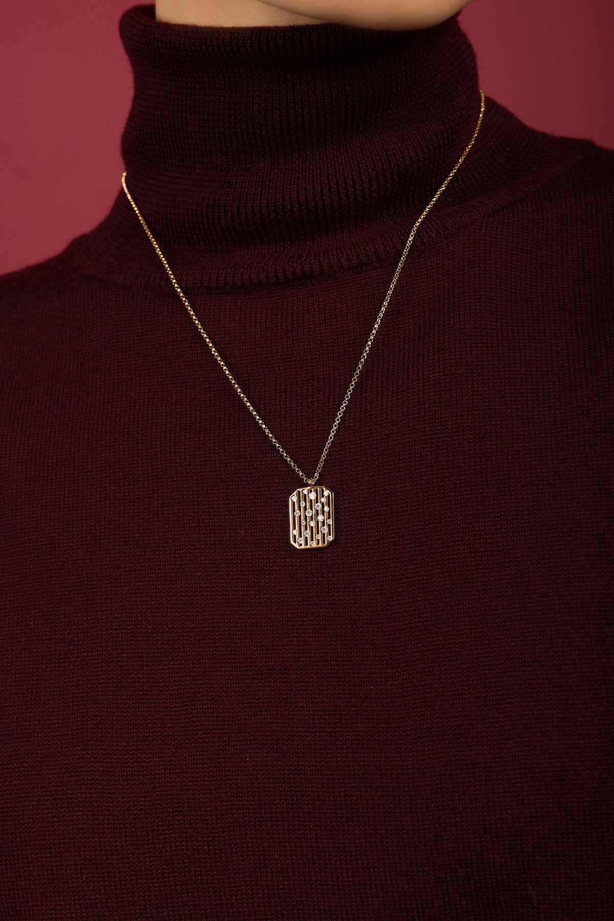 Woman wearing APM pendant necklace, a golden whisper against burgundy warmth.