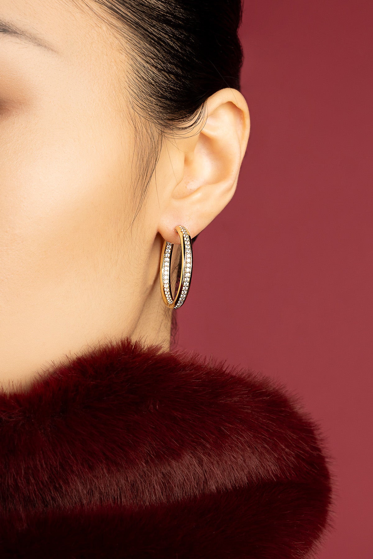 Woman wearing APM hoop earrings, a golden shimmer against deep burgundy elegance.