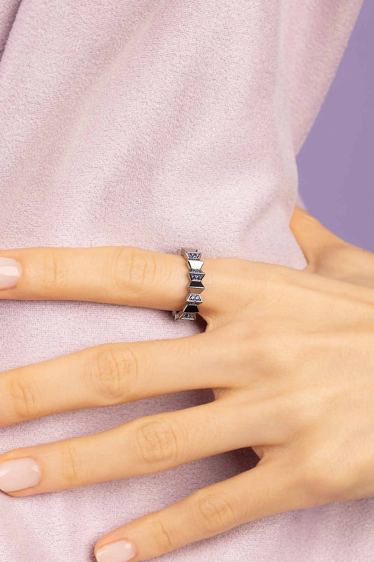 Hand wearing a silver ring on a light pink background