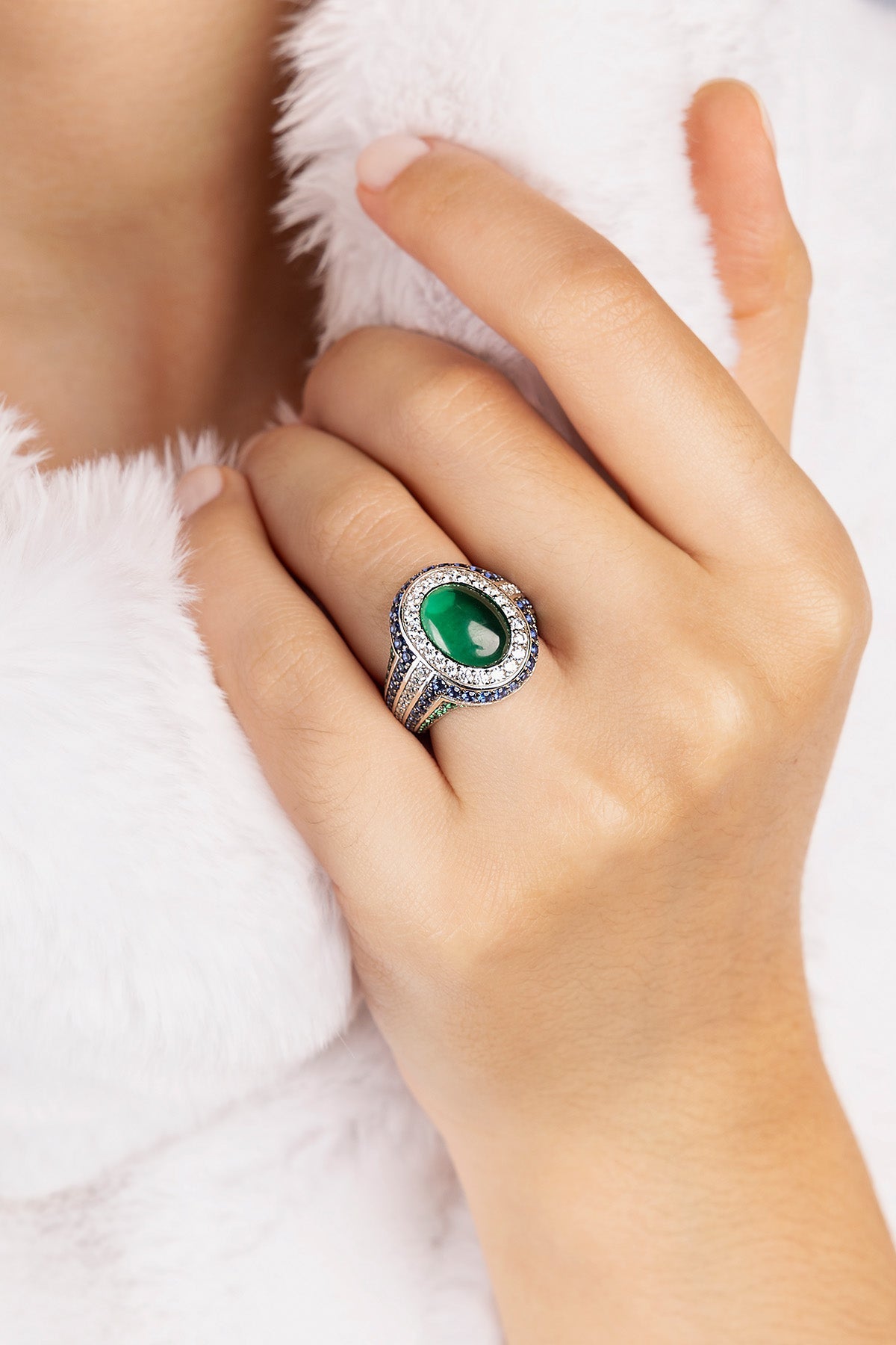 Hand wearing a ring with a green gemstone on a white background