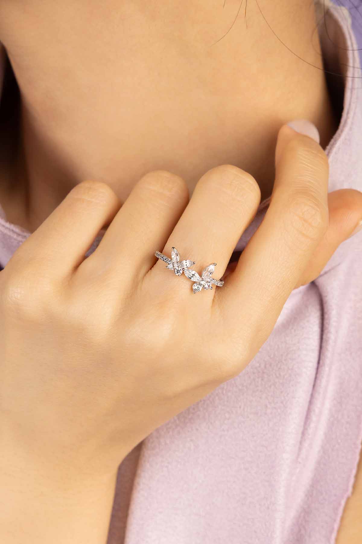 Close-up of a hand wearing a silver ring with butterfly design on a light background