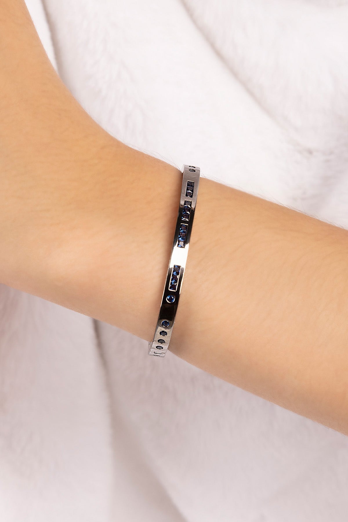 Silver bracelet with blue stones on a wrist against a white background
