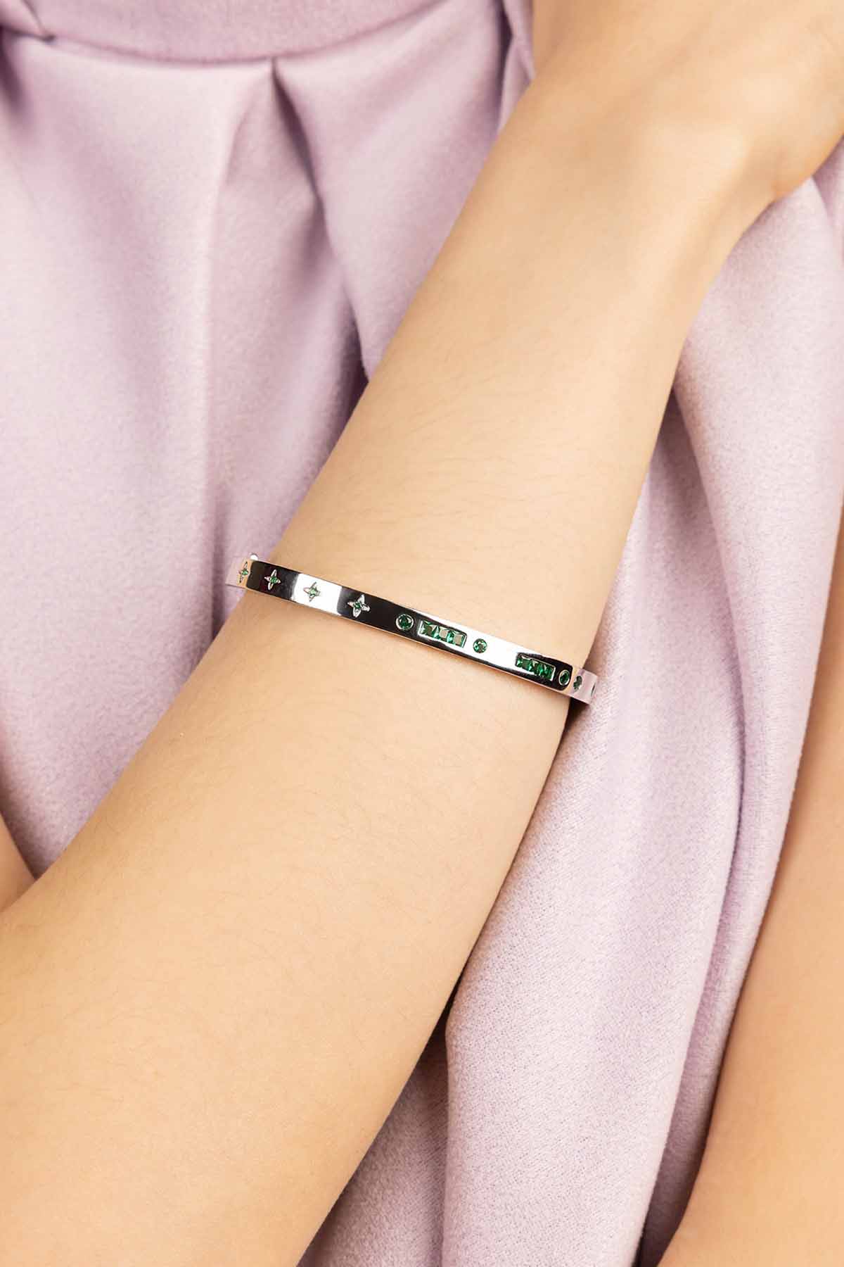 Silver bracelet with green stones on a person's wrist against a pink fabric background