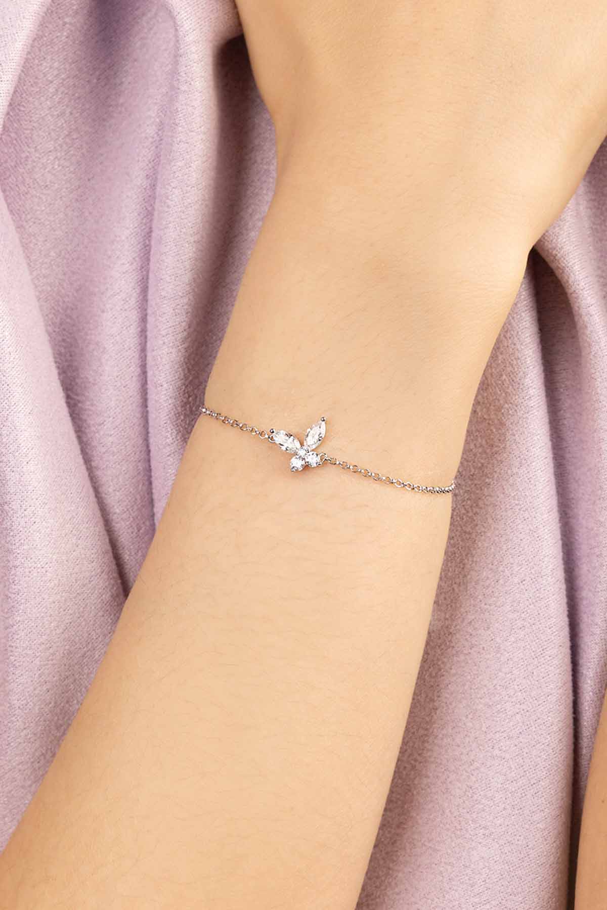 Silver bracelet with a butterfly-shaped clasp on a wrist against a soft pink fabric background