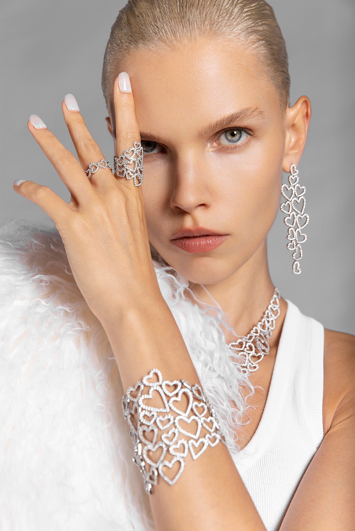 Woman wearing APM MONACO heart-shaped jewelry in silver, including rings, earrings, and bracelet against a neutral background