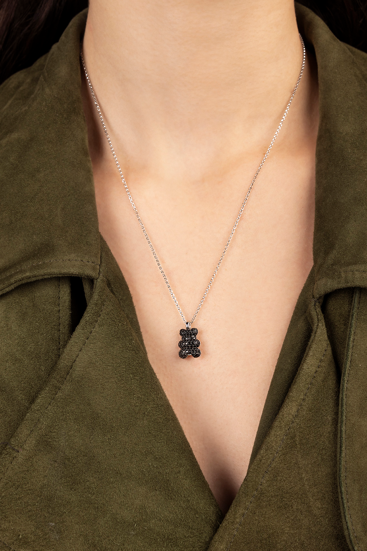 APM MONACO Necklace with a black yummy bear pendant worn by a person in an olive green jacket.