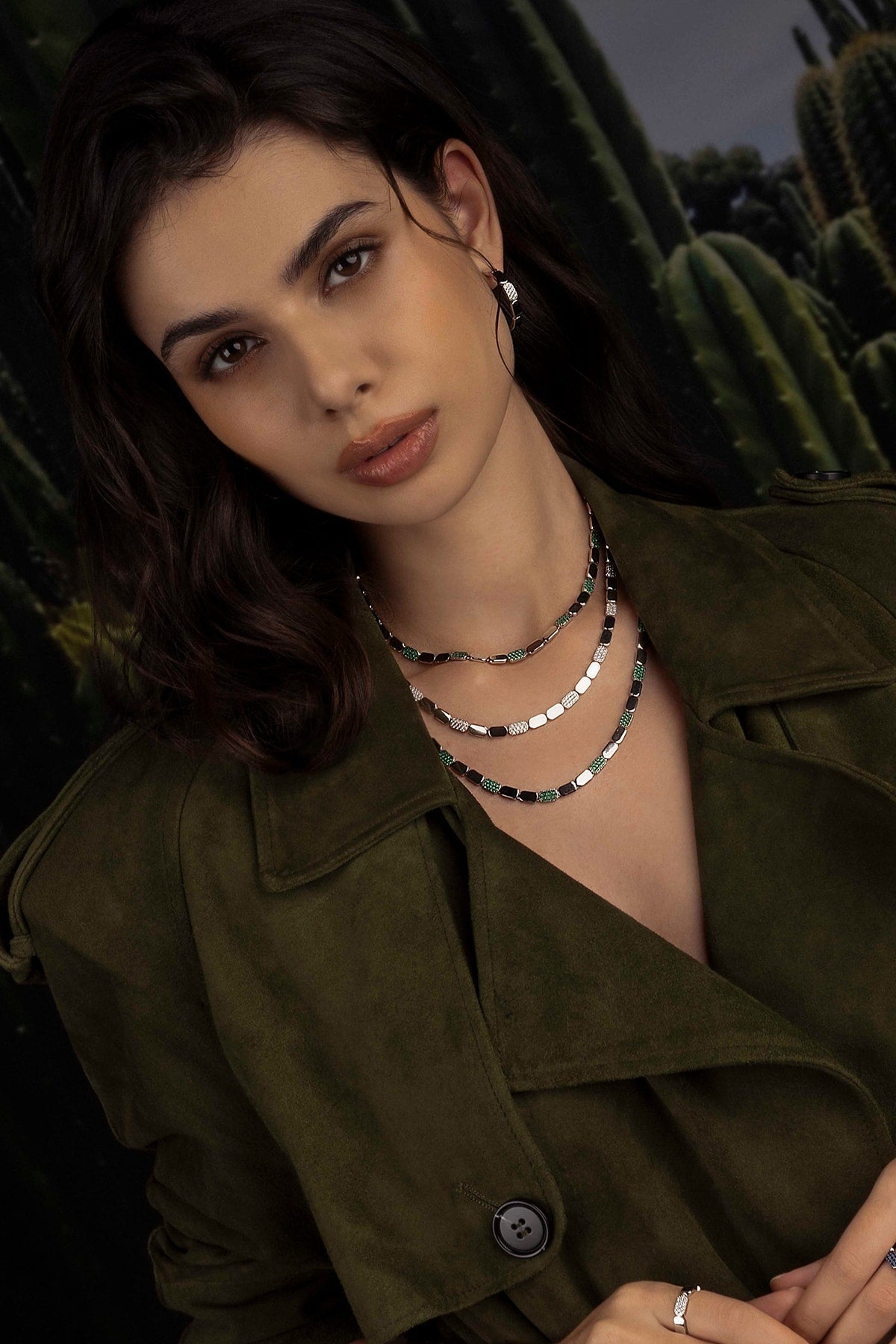 Model wearing a green jacket and layered necklaces with cacti in the background