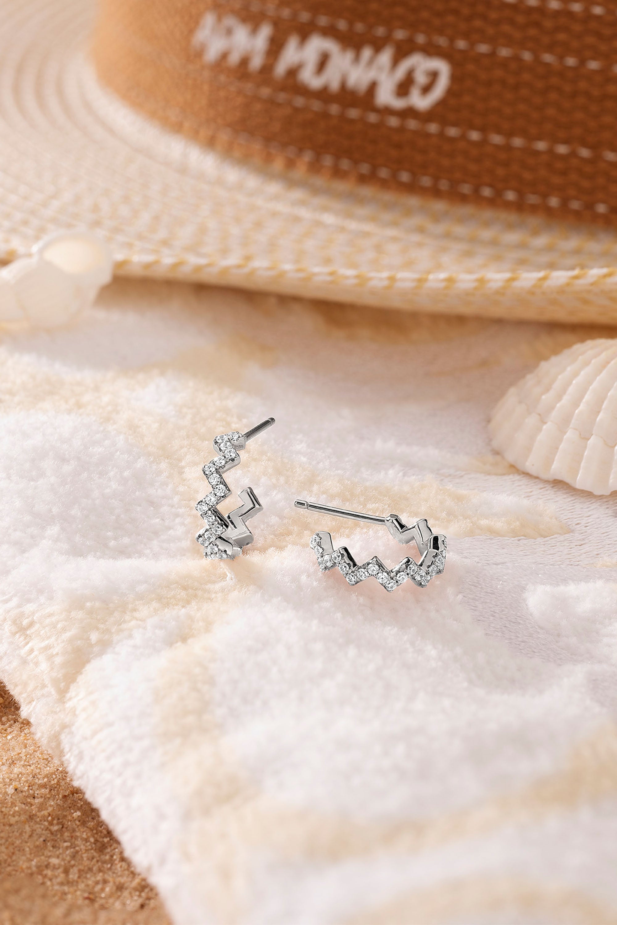 Sterling silver pavé zigzag earrings on beach towel with a hat and shell