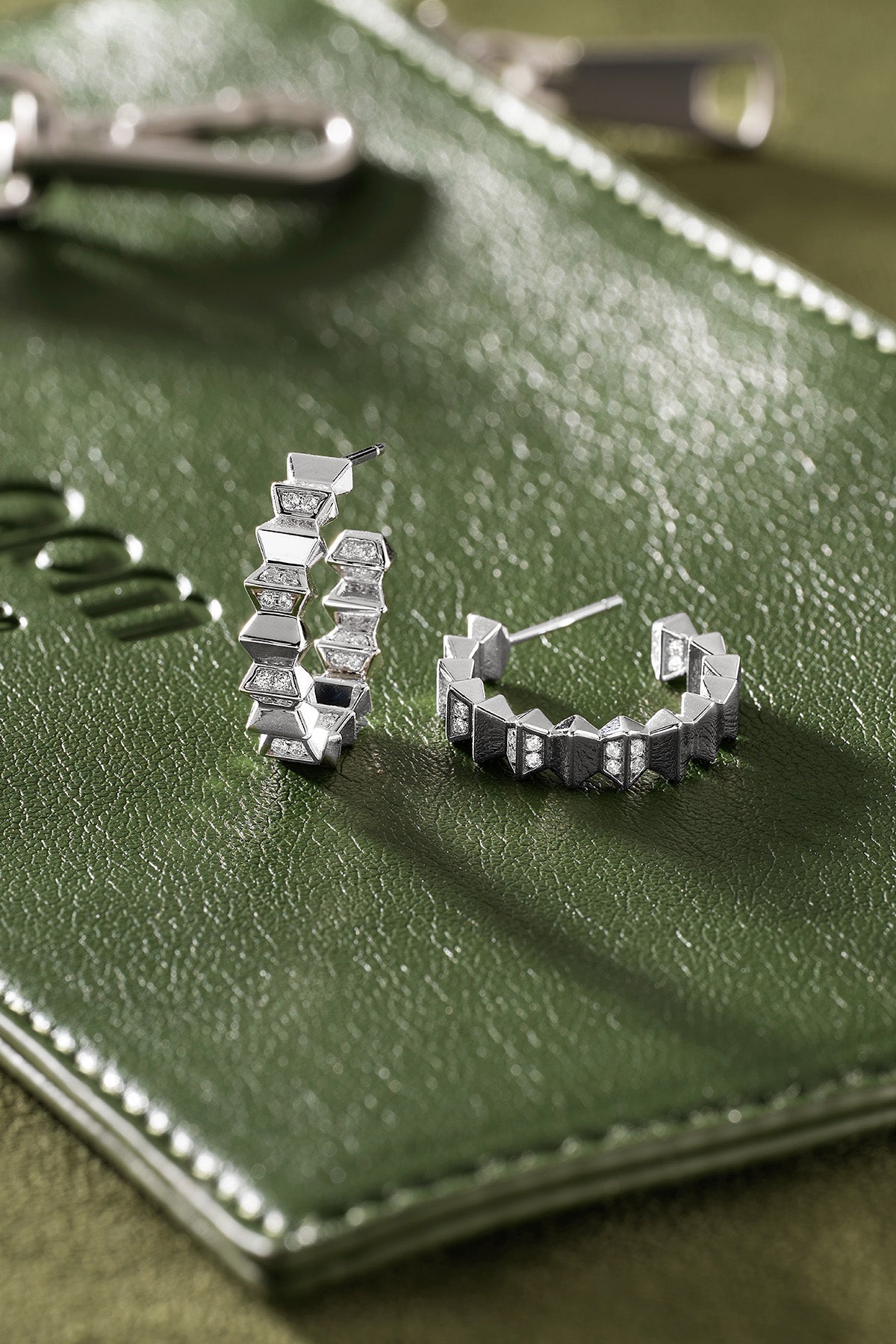 Silver hoop earrings on a green leather surface