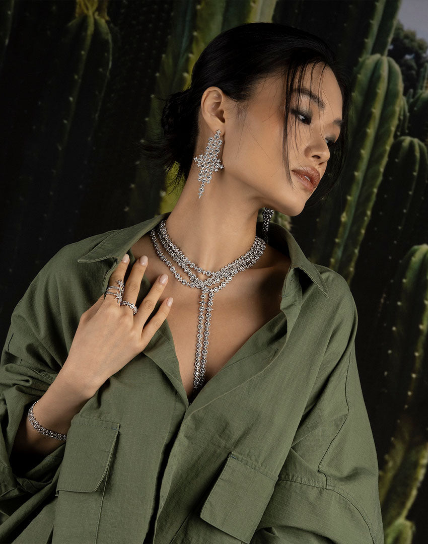Woman wearing a green outfit with apm monaco Meteorites jewelry against a cactus background, including earrings, necklace, bracelets and rings
