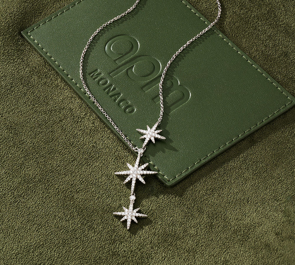APM MONACO Meteorites collection - triple star-shaped necklace on a green textured surface with 'APM Monaco' branding.