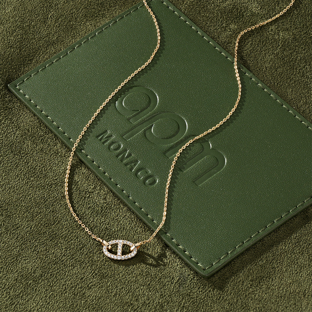 APM MONACO gold yacht club unisex necklace on a green textured bag surface