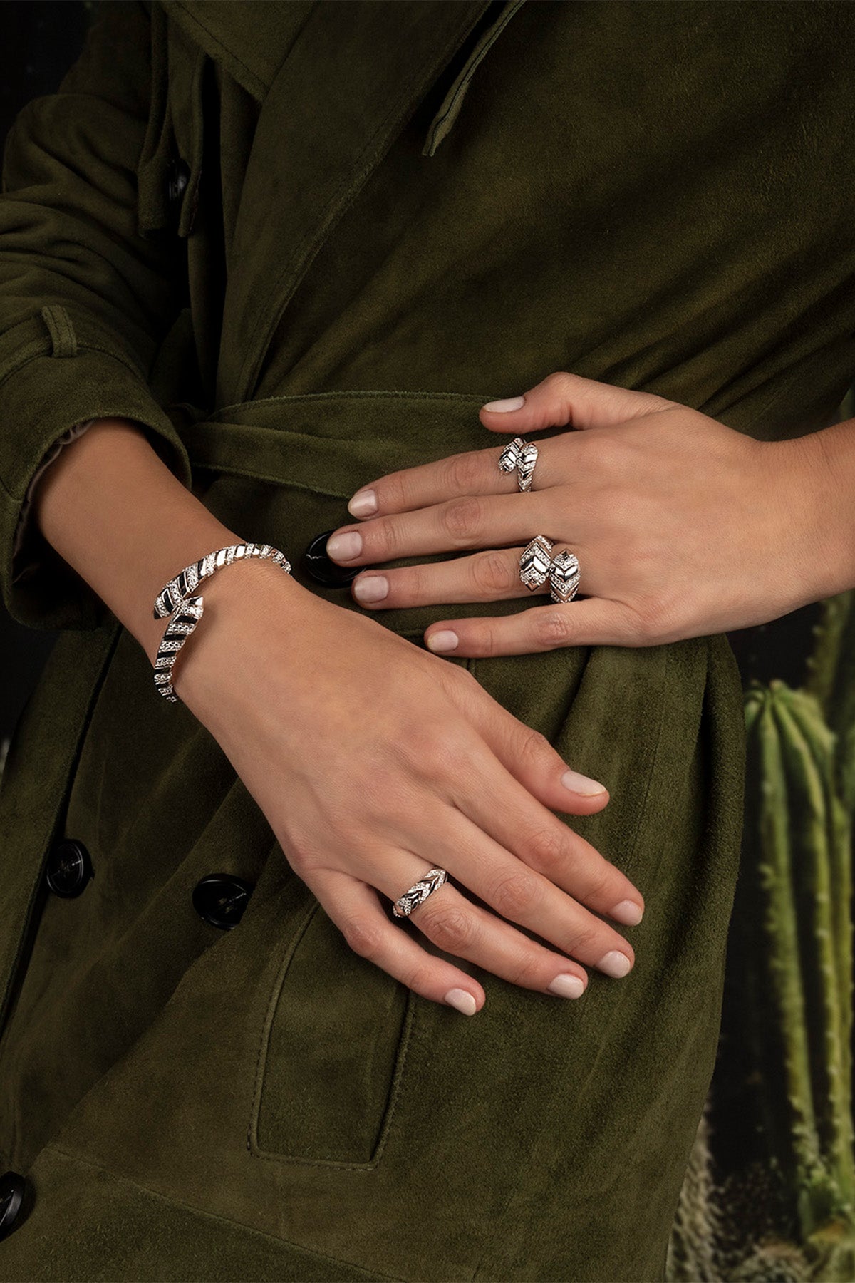 Close-up of hands wearing multiple APM MONACO KAA rings on a green fabric background