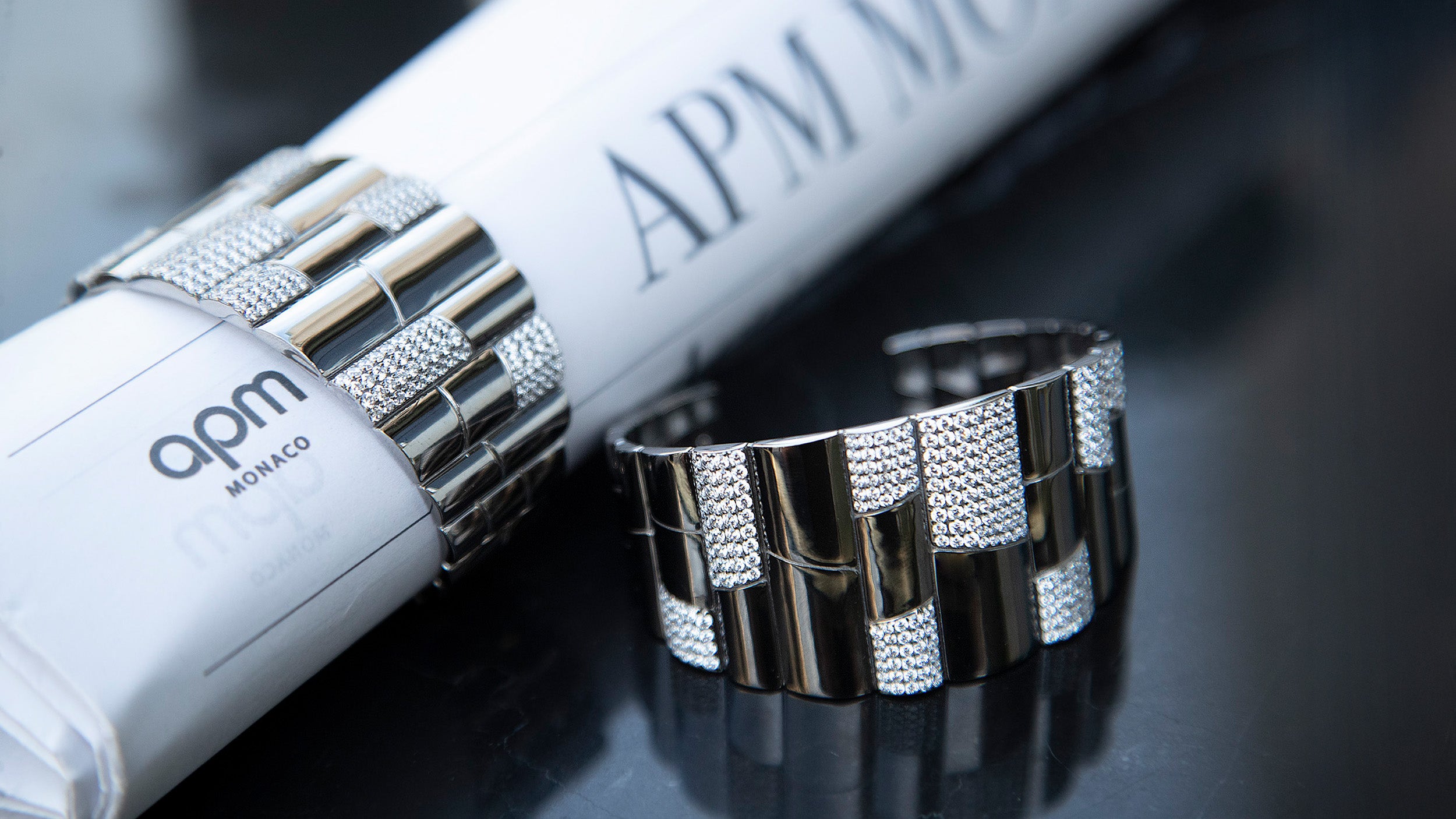 APM MONACO silver pave bangle with 'apm monaco' branding name on a reflective surface