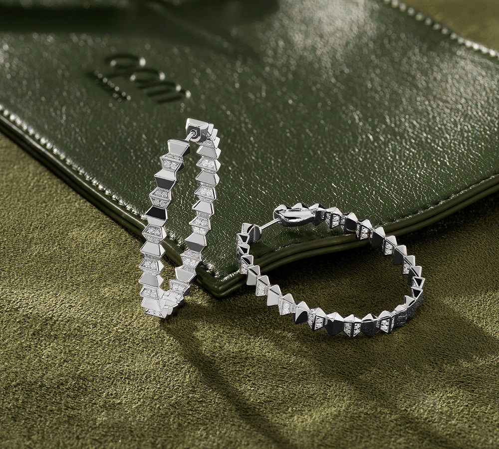 APM MONACO up and down hoop earrings in silver on a khaki textured surface