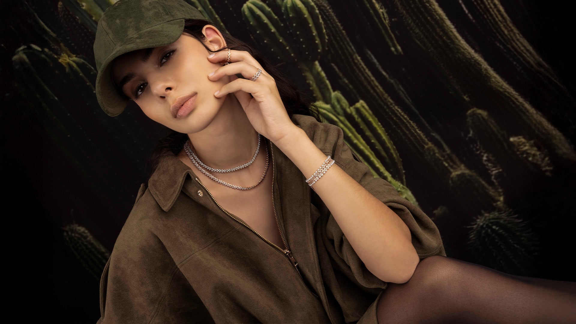Woman wearing a green cap with APM MONACO jewels from up and down pearl collection, against a dark background with cacti.
