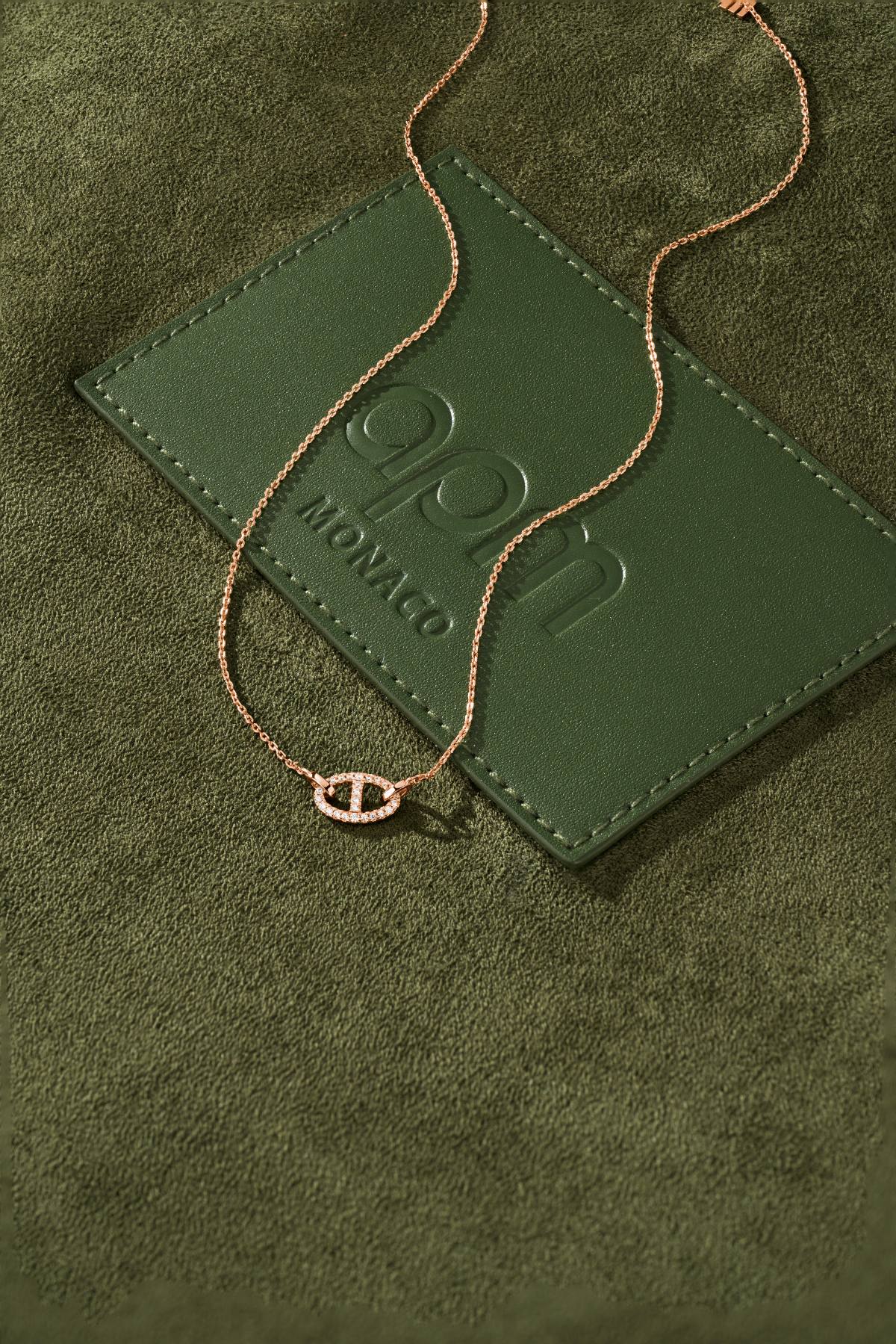 Rose gold necklace on a green textured surface with 'APM Monaco' branding.
