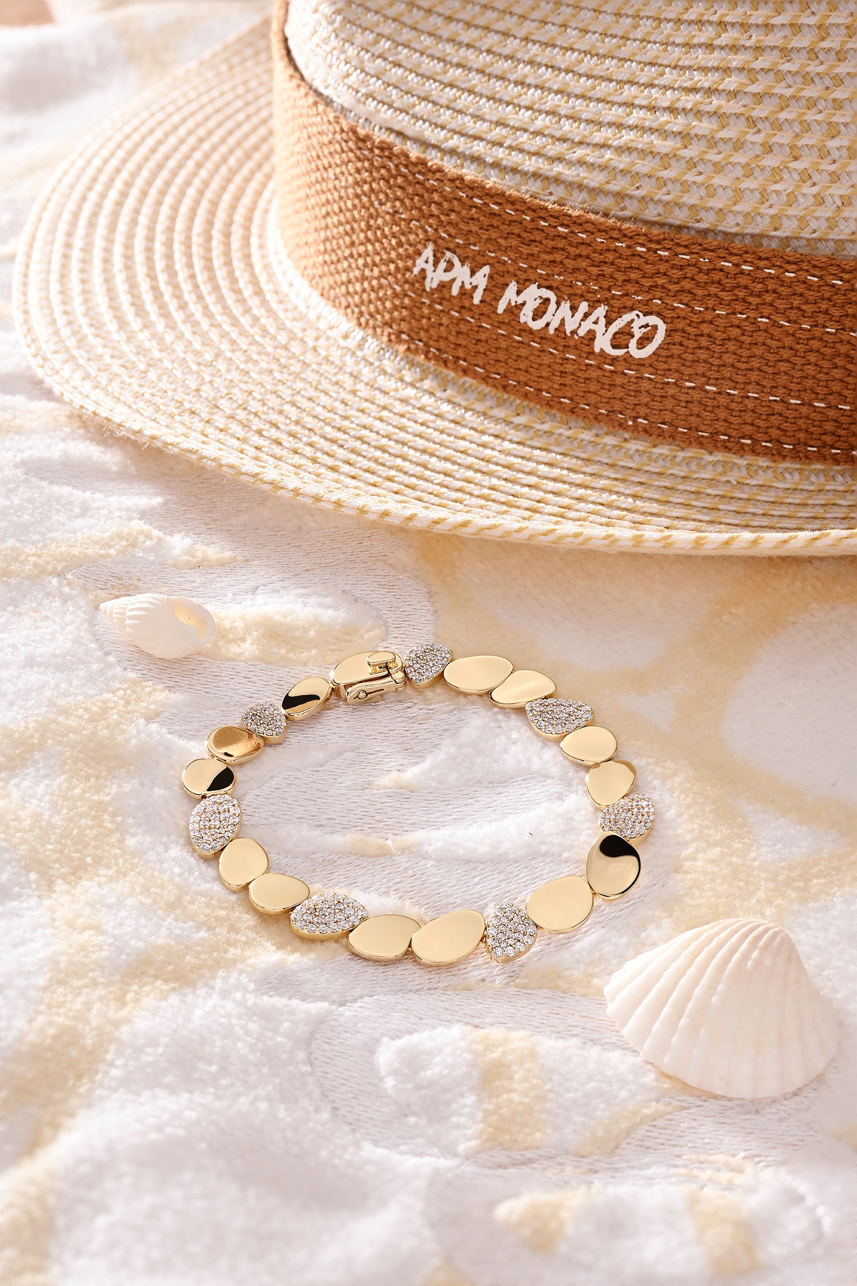 Gold-plated bracelet on sand with APM Monaco hat in the background