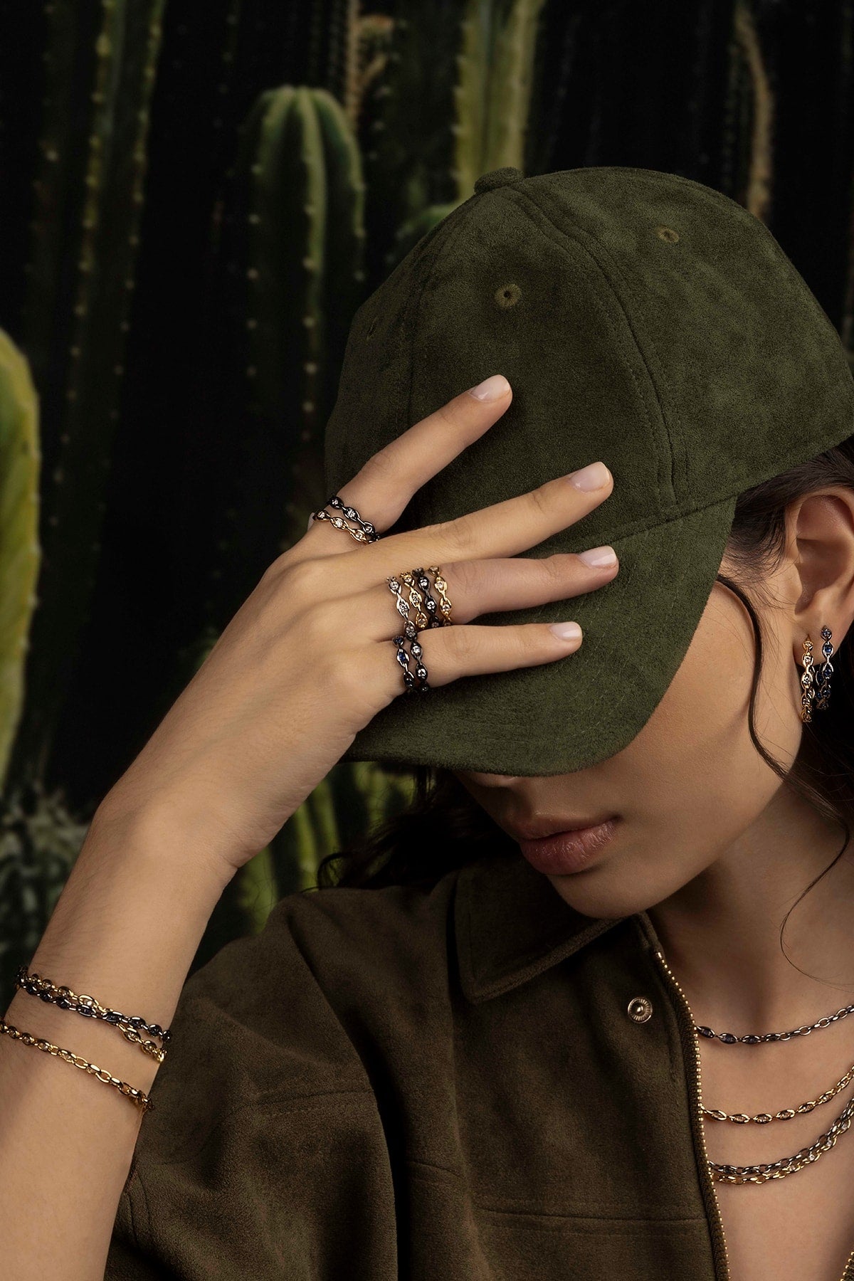 Person wearing a green cap and jewelry with cacti in the background