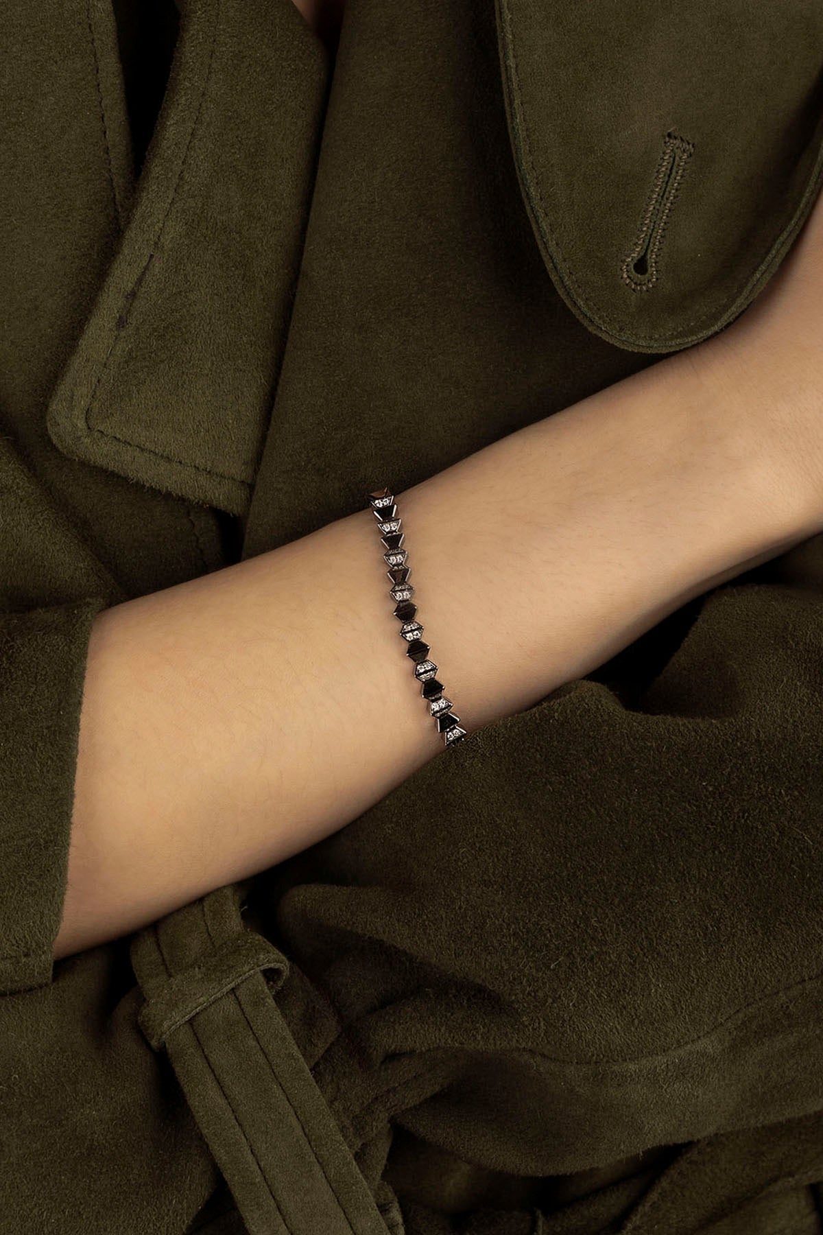 APM MONACO up and down bracelet in silver on a wrist with a dark khaki coat in the background