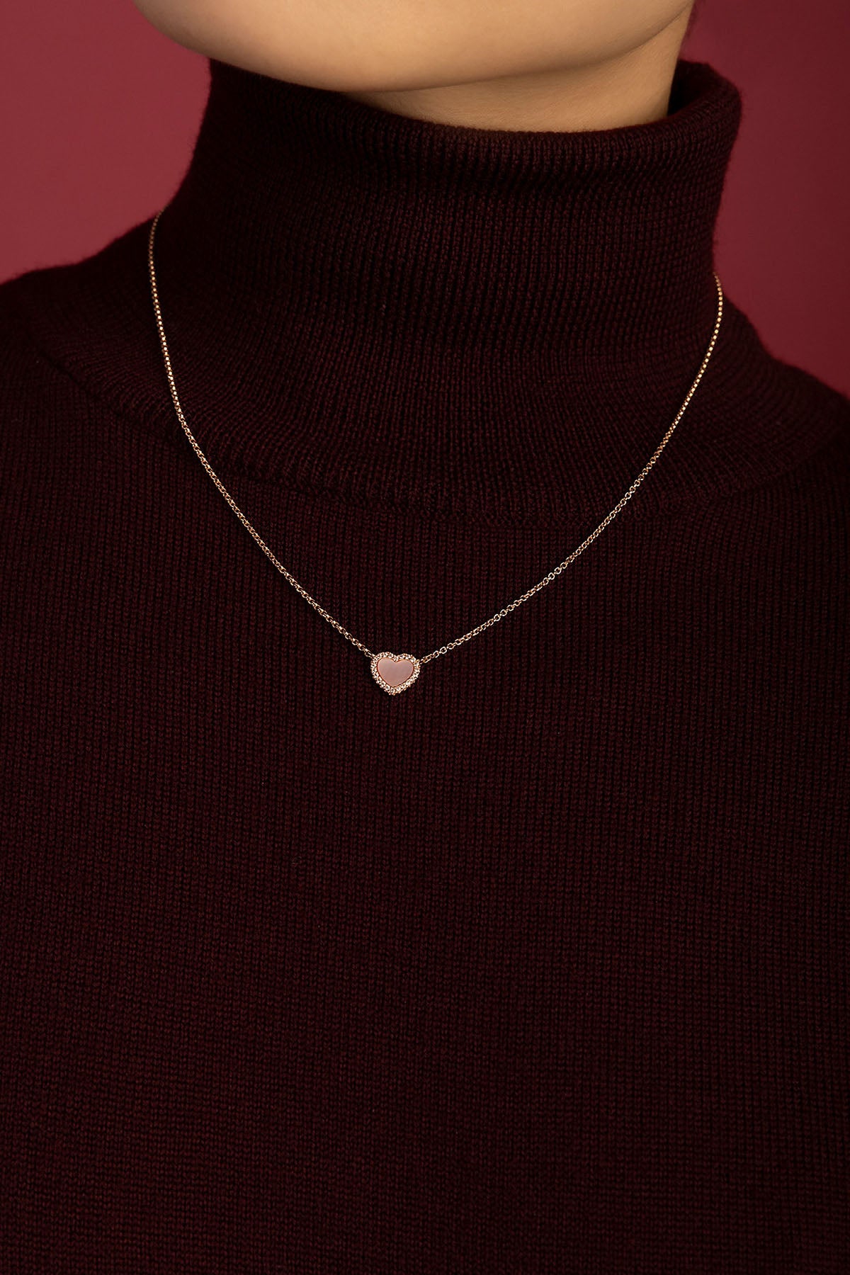 Woman wearing APM heart necklace, a tender glow against burgundy warmth.