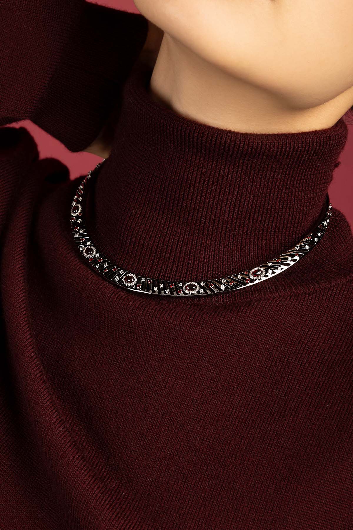 Woman wearing APM Monaco necklace, a bold statement against burgundy warmth.
