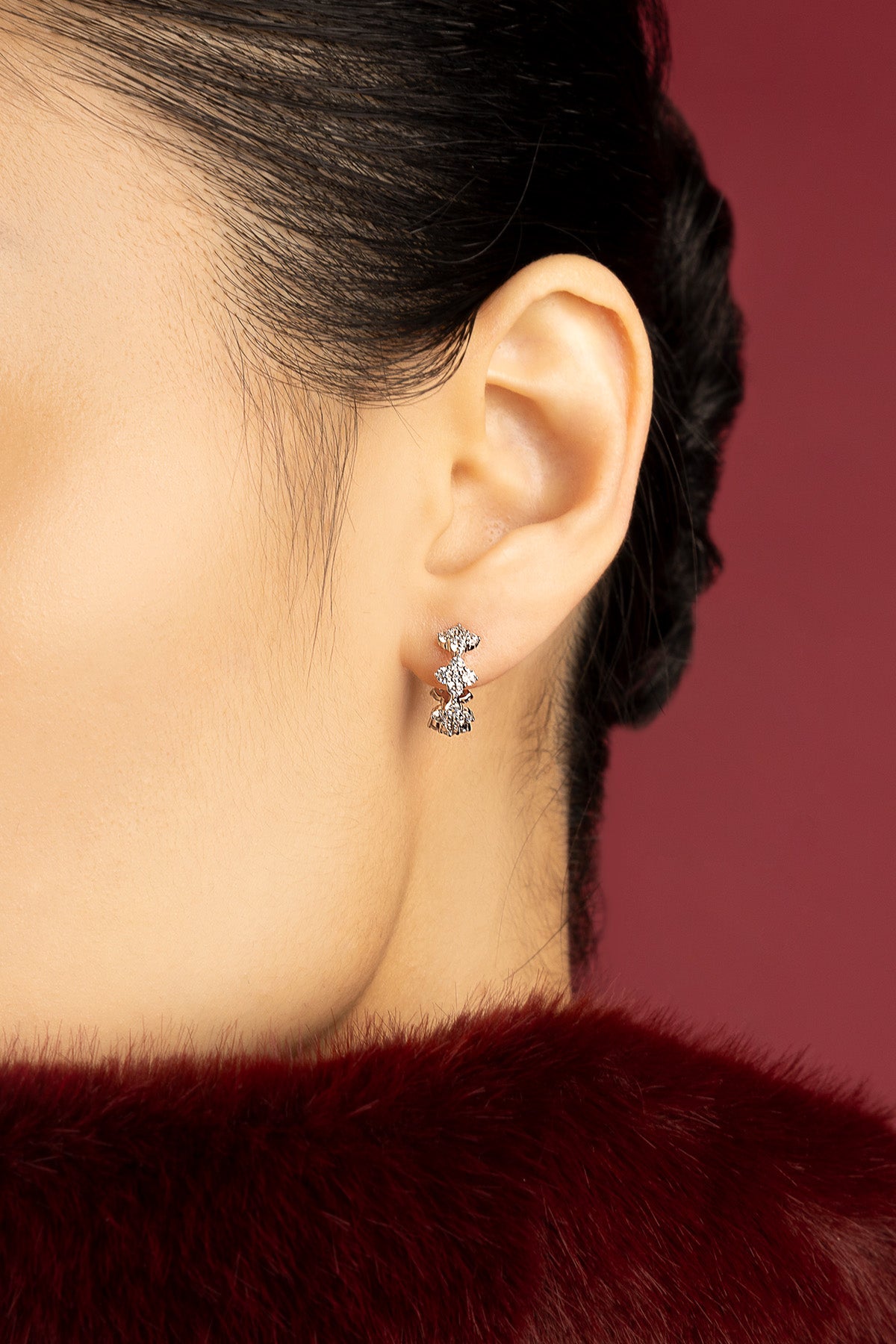 Woman wearing APM earrings, a playful sparkle against crimson elegance.