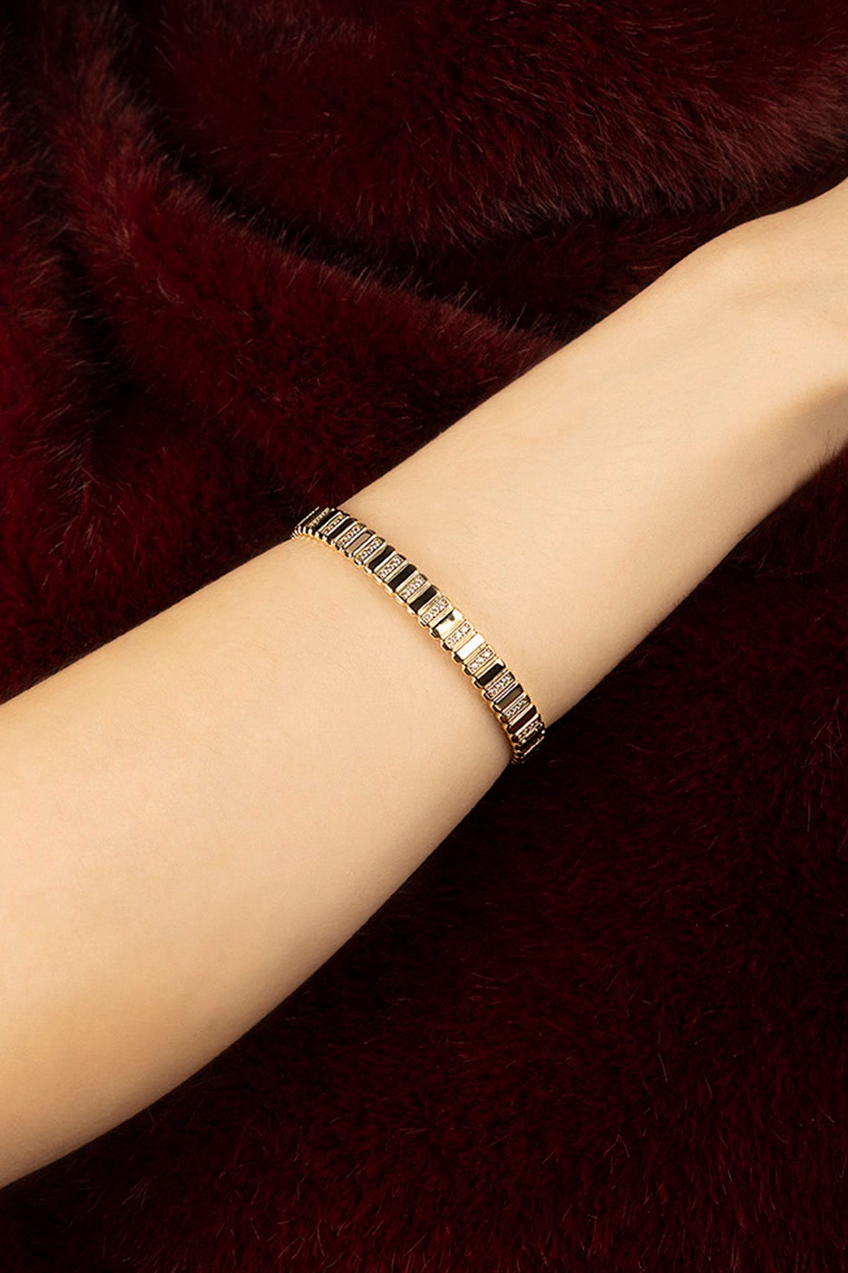 Woman wearing APM bracelet, a golden whisper against velvet warmth.