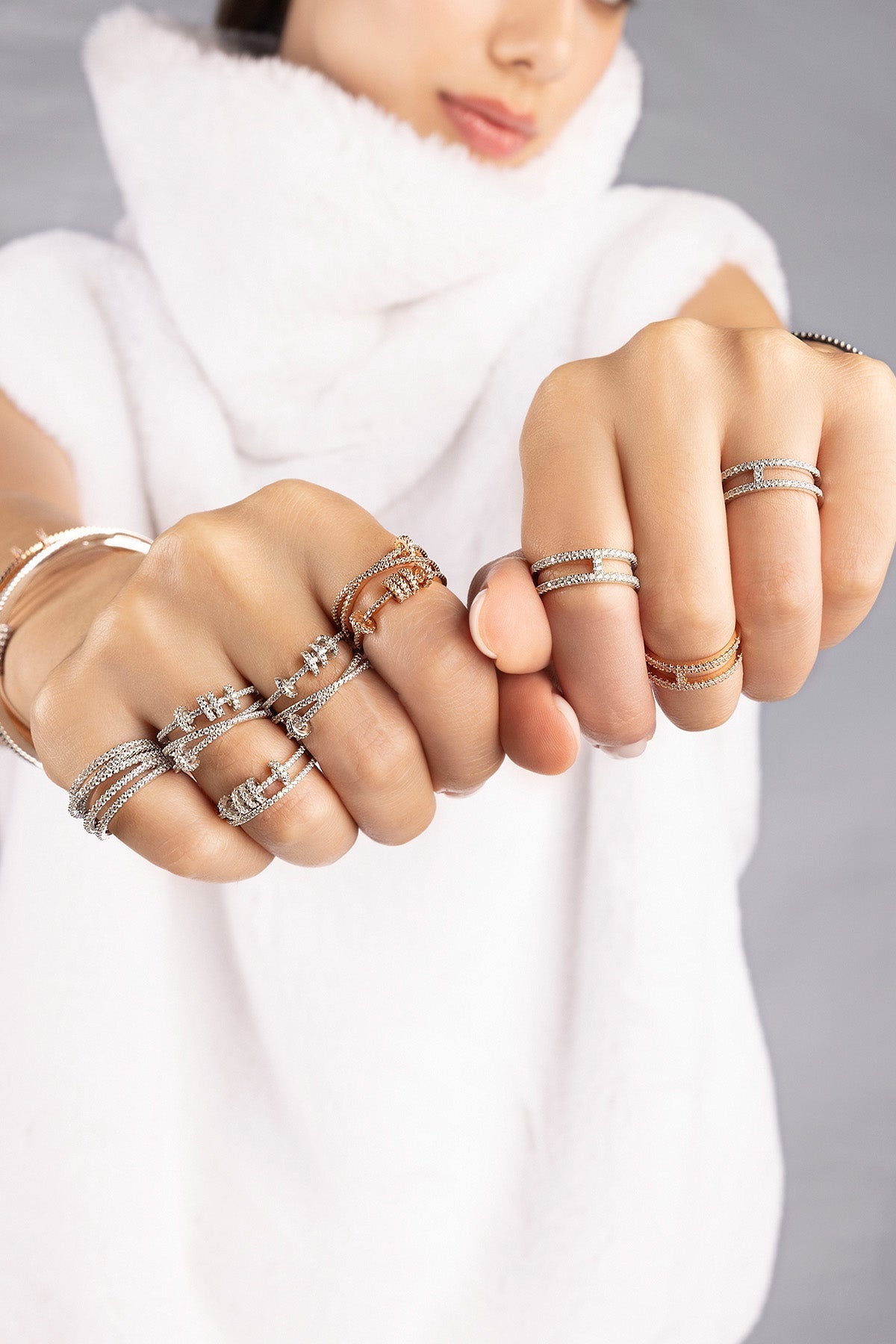 Close-up of hands wearing multiple APM MONACO silver rings with sliding hoops design on a plain background