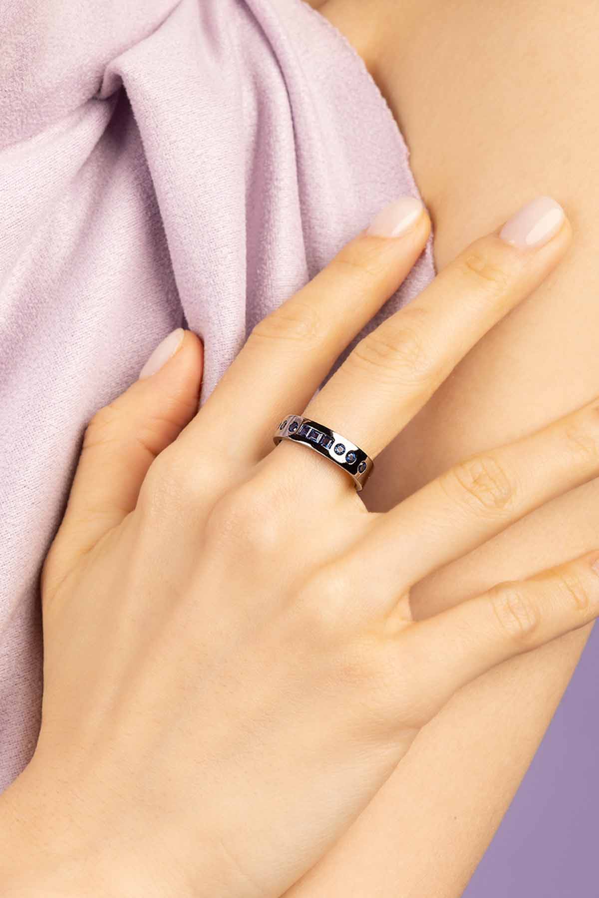 Close-up of a hand wearing a ring with embedded stones on a light pink fabric background