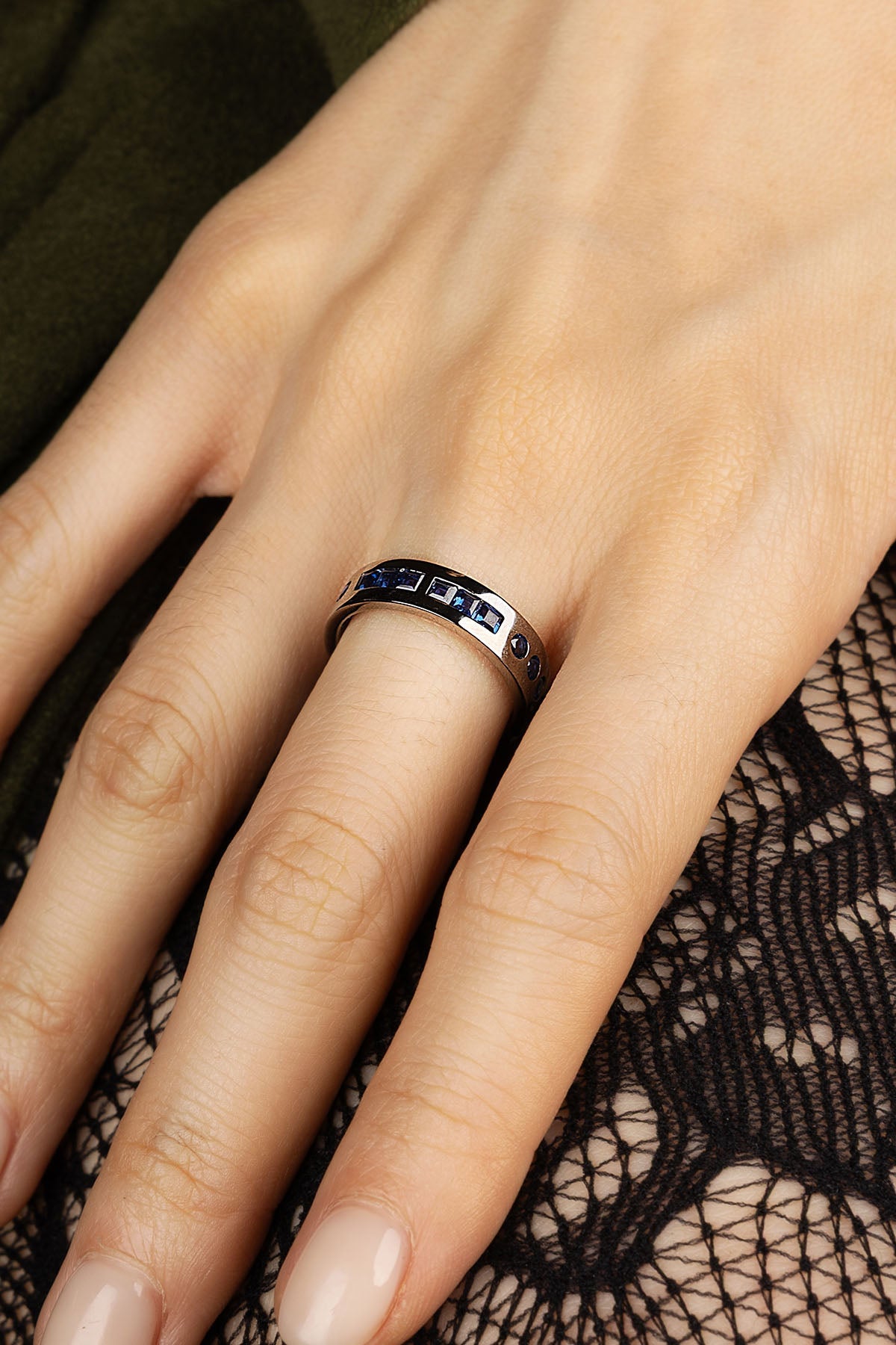 Close-up of a hand wearing a silver ring with blue accents on a black lace background