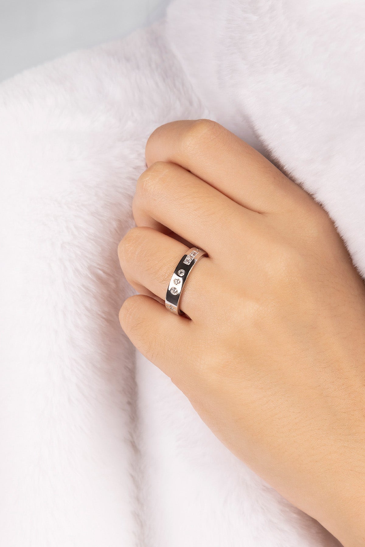 Hand wearing a silver ring with small stones on a white background