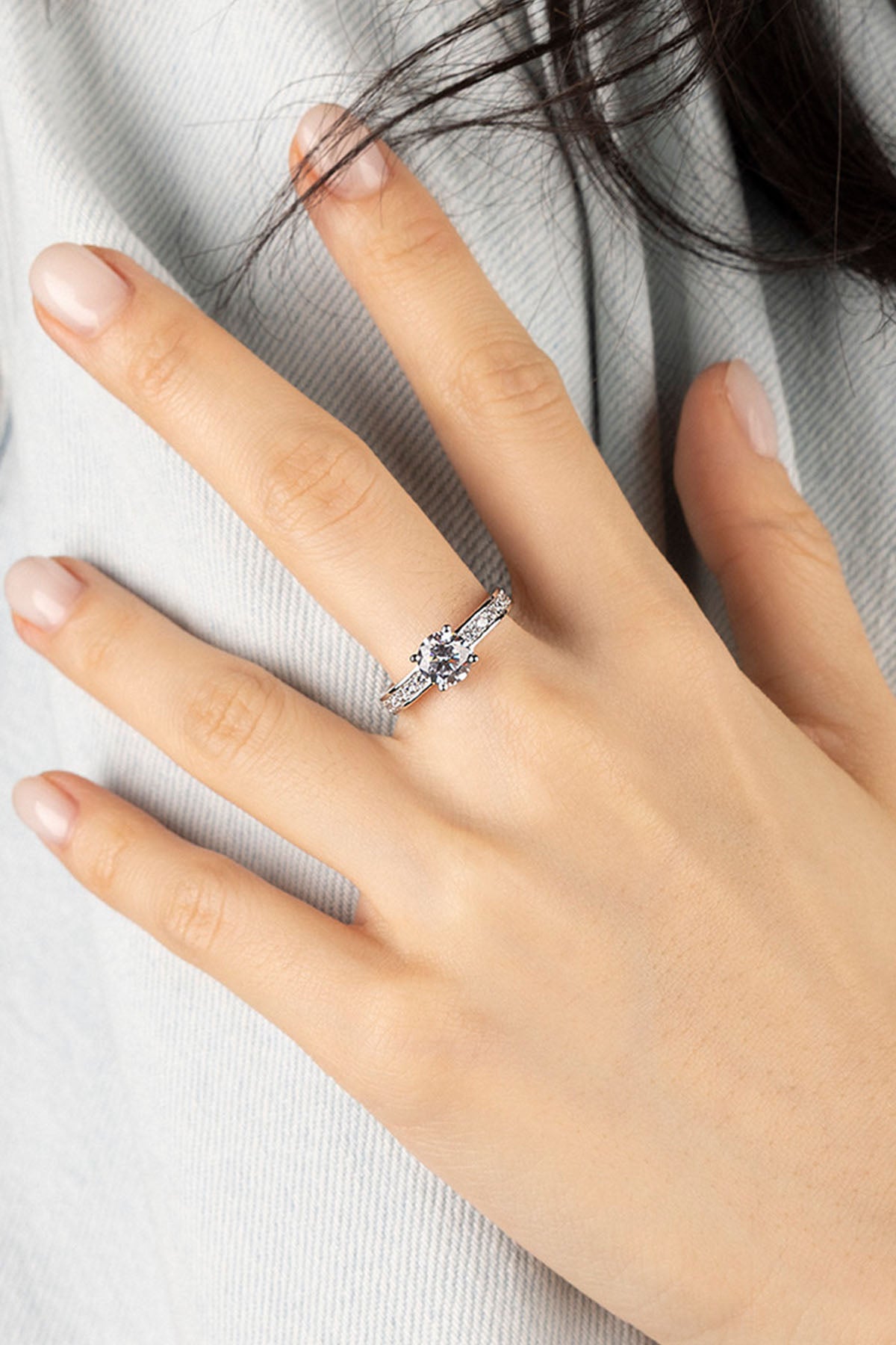 Hand wearing a silver ring on a light gray fabric background