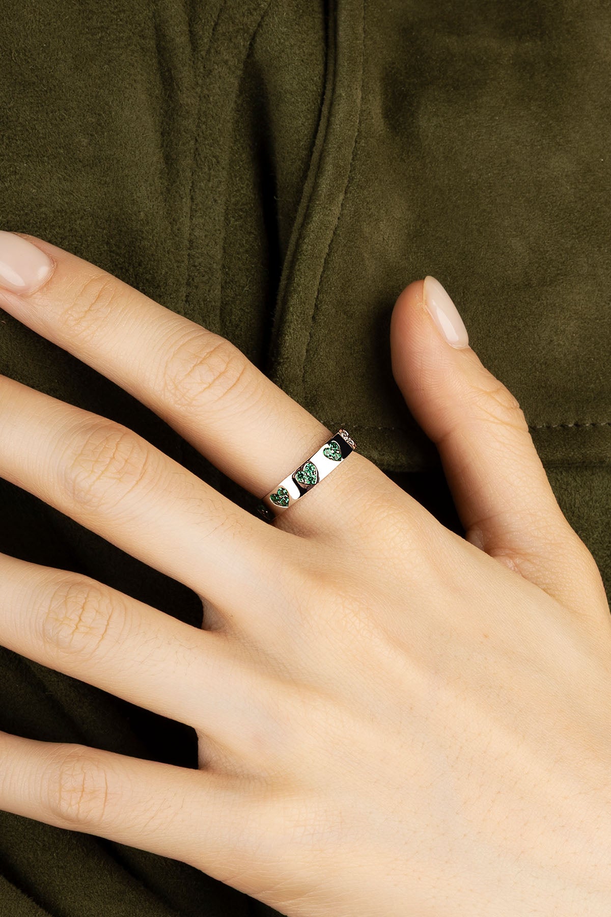 Close-up of a hand wearing a silver ring with green gemstones on a dark fabric background
