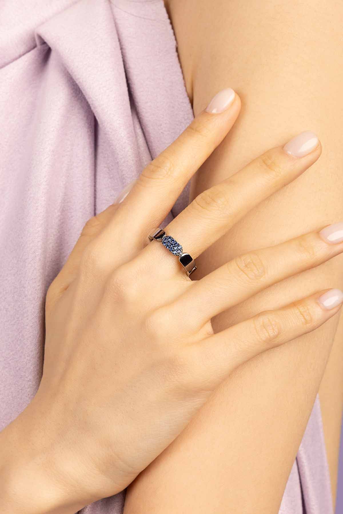 Hand wearing a ring with blue gemstones on a light pink fabric background