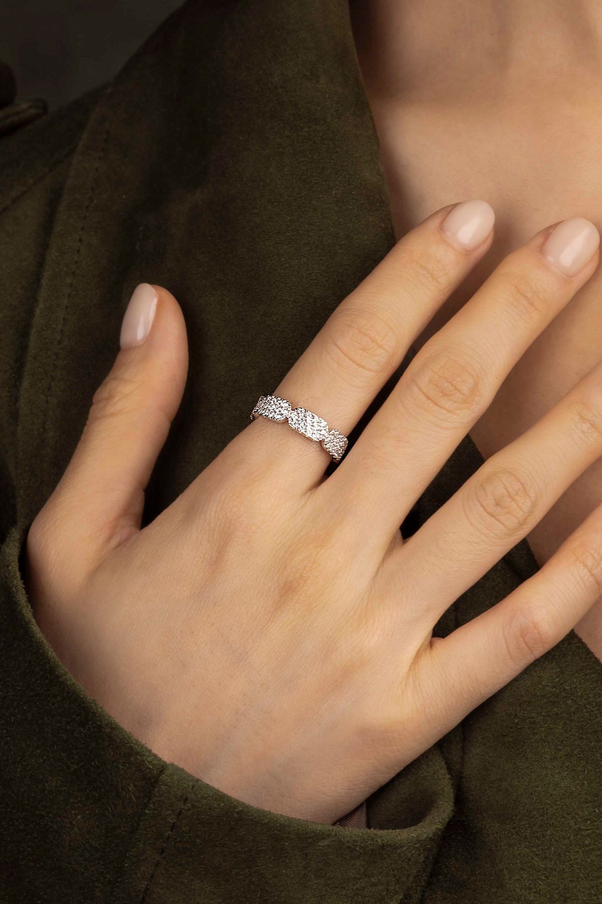 A hand wearing a silver ring on a warm background