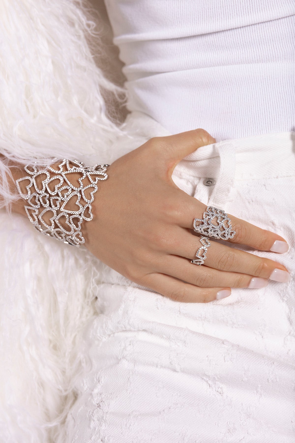 Close-up of a hand wearing APM MONACO heart-shaped silver jewelry on a white background
