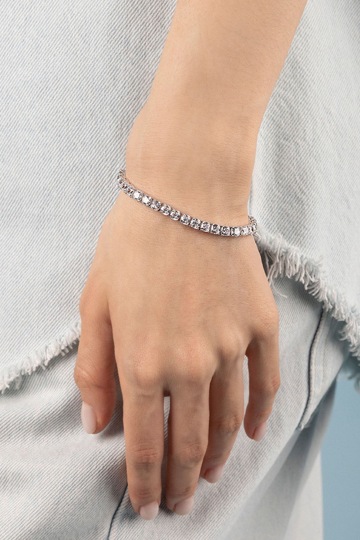 Hand wearing a silver bracelet on a light gray background