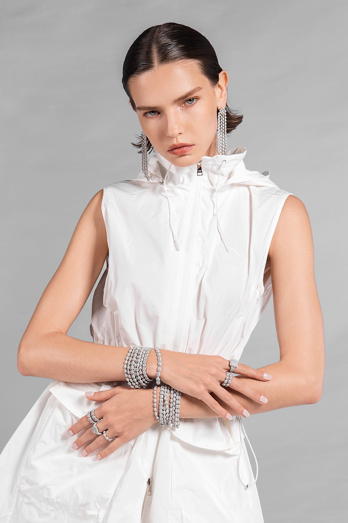 Model wearing a white sleeveless dress with APM MONACO pave jewelry on a gray background