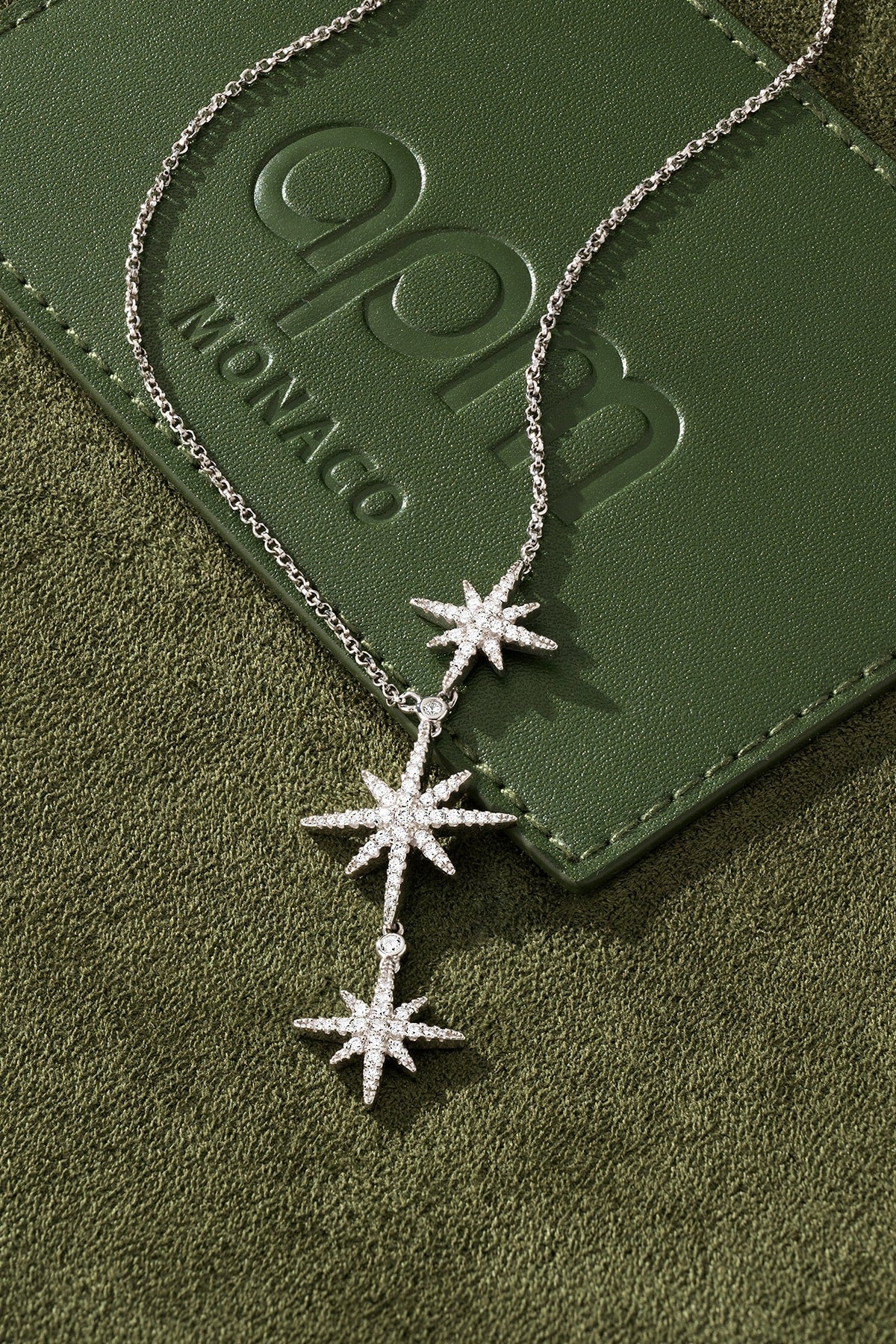 Silver star-shaped necklace on a green textured surface with 'APM Monaco' branding.