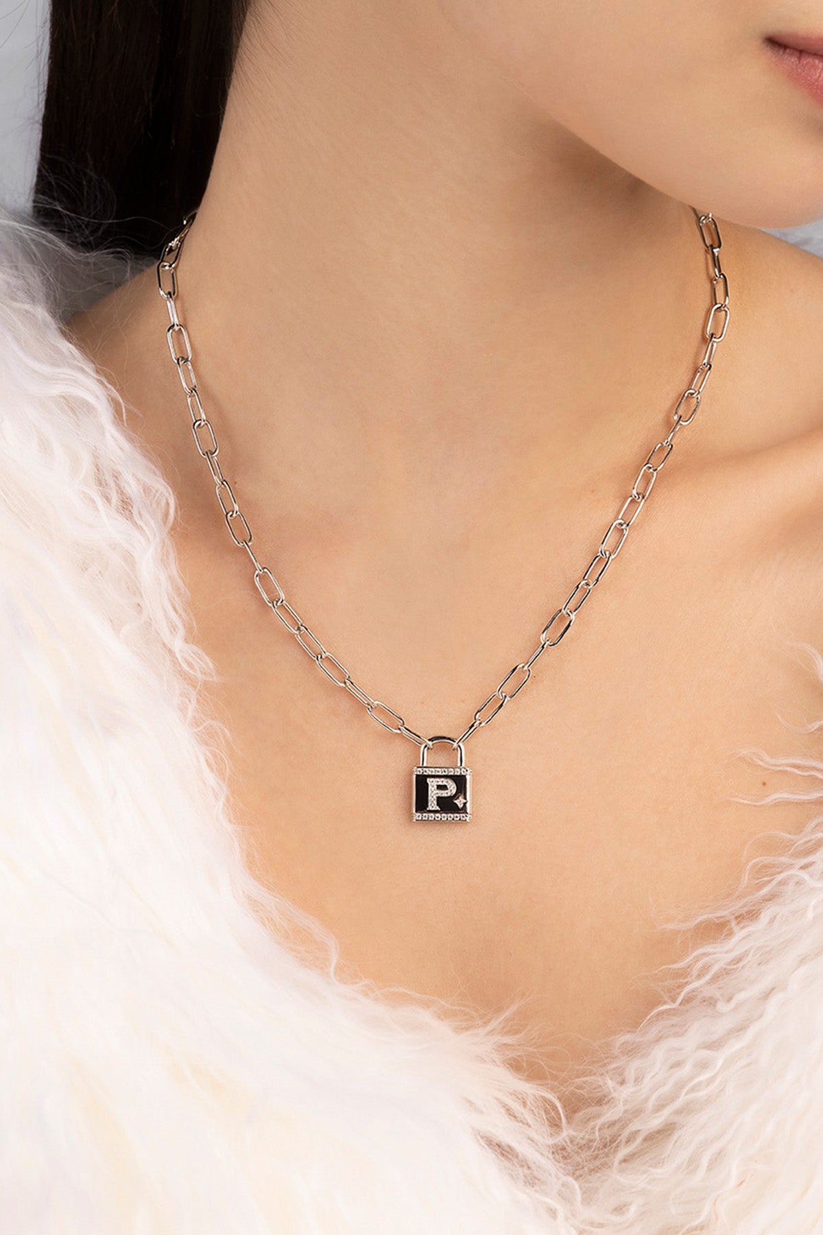 Necklace with a lock pendant featuring a letter 'P' worn by a person with white outfit