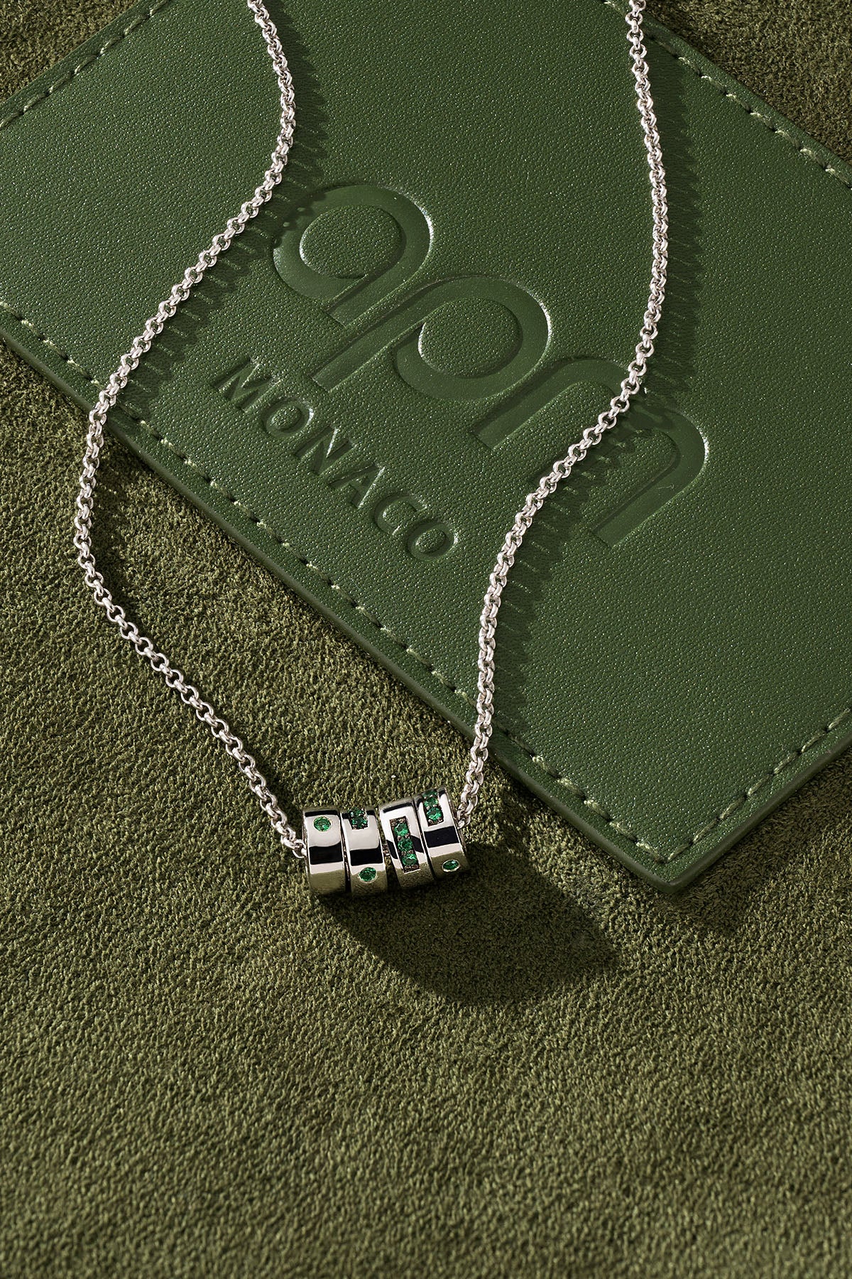 Silver necklace with a pendant on a green leather surface 