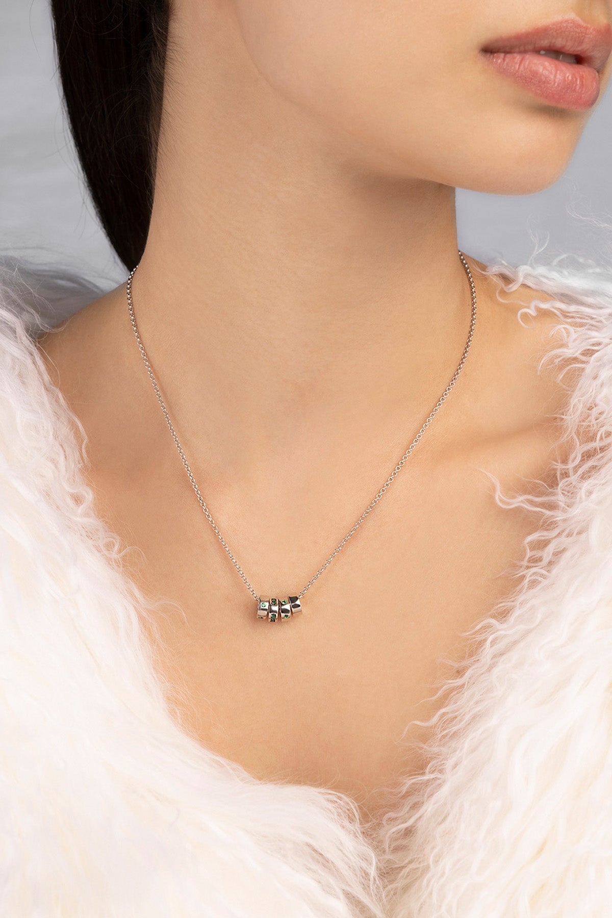 Necklace with a small pendant worn by a person in a white fur garment.