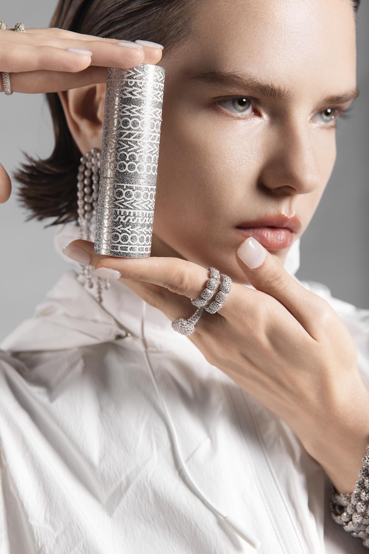 Woman holding a lip balm with intricate designs, wearing multiple silver rings on fingers.
