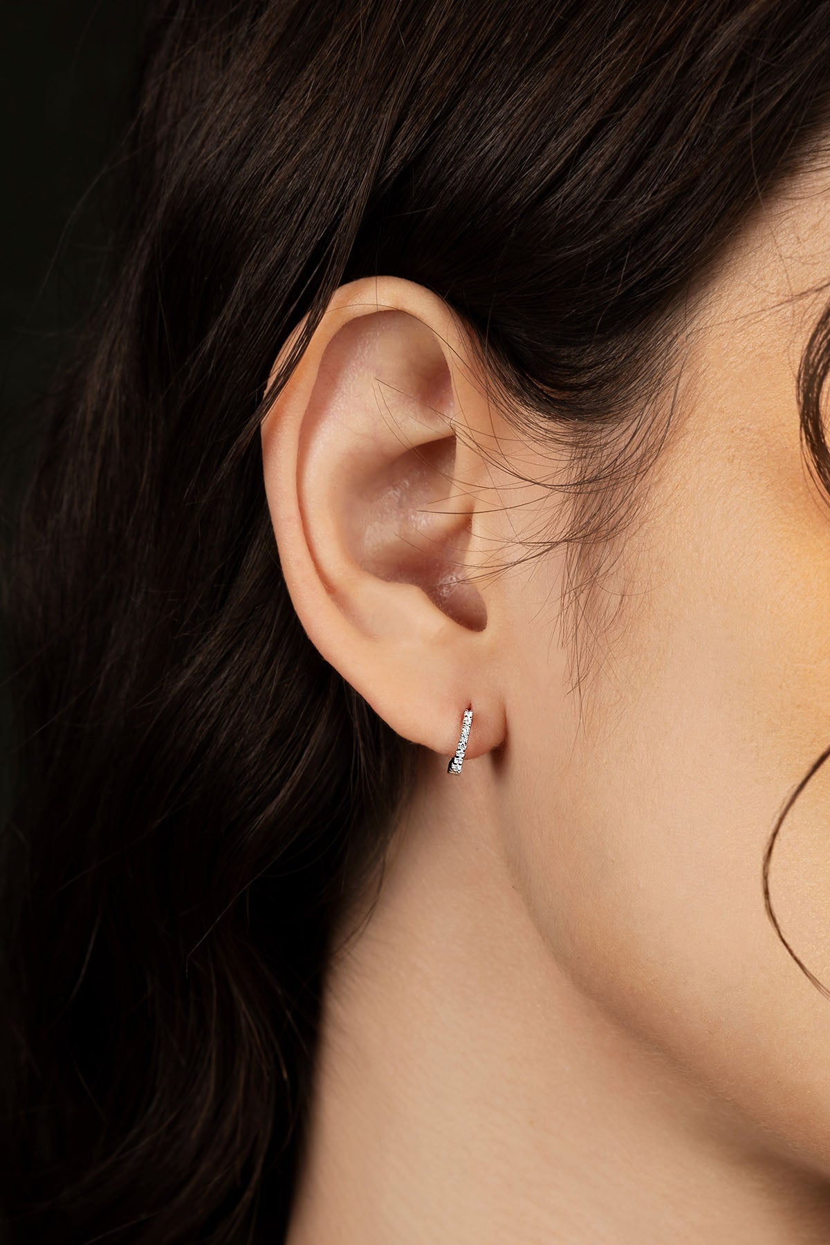 Close-up of an ear wearing a earring with dark hair and skin in the background