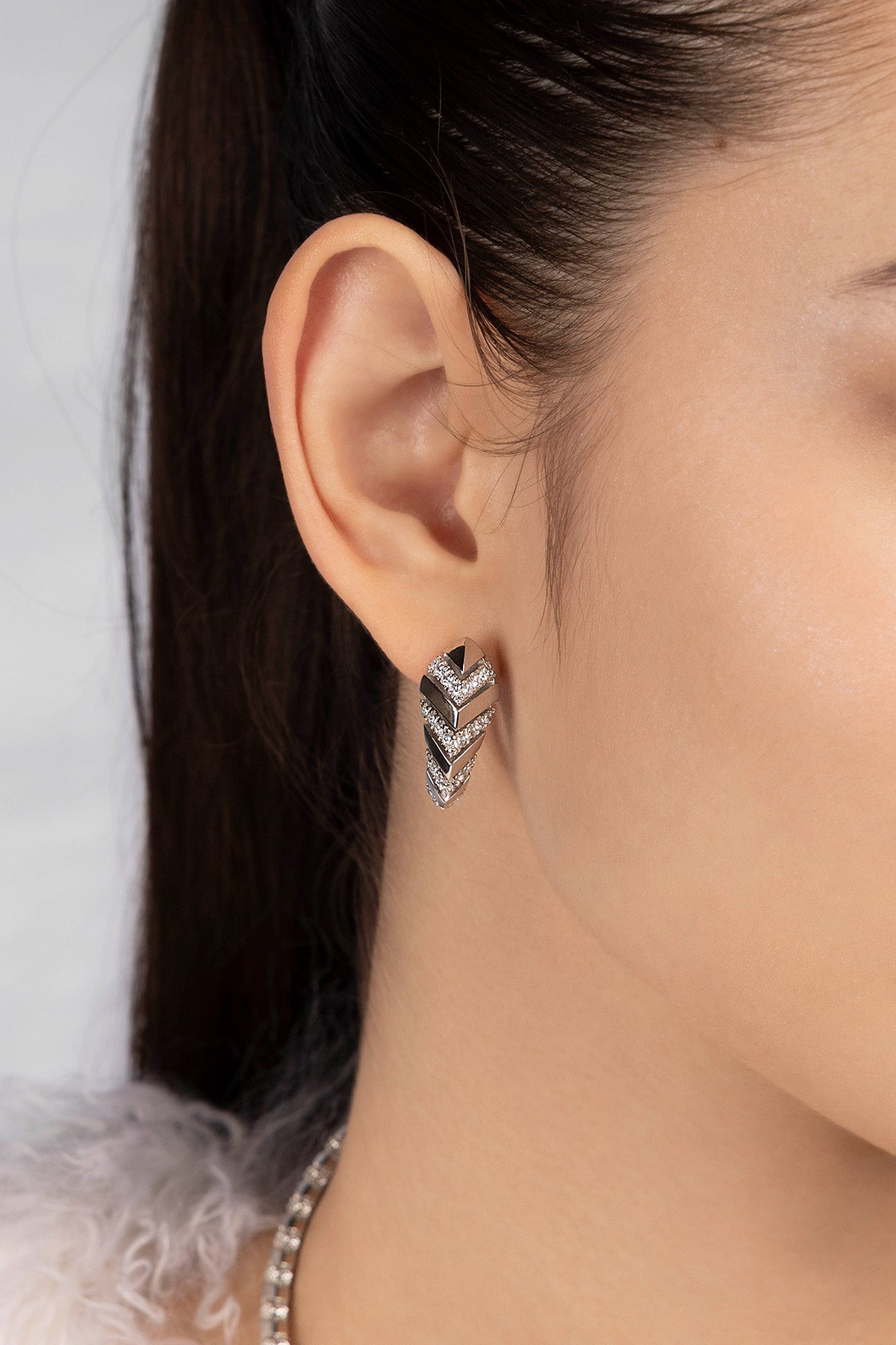 Close-up of an ear wearing a silver zigzag earring with a blurred background