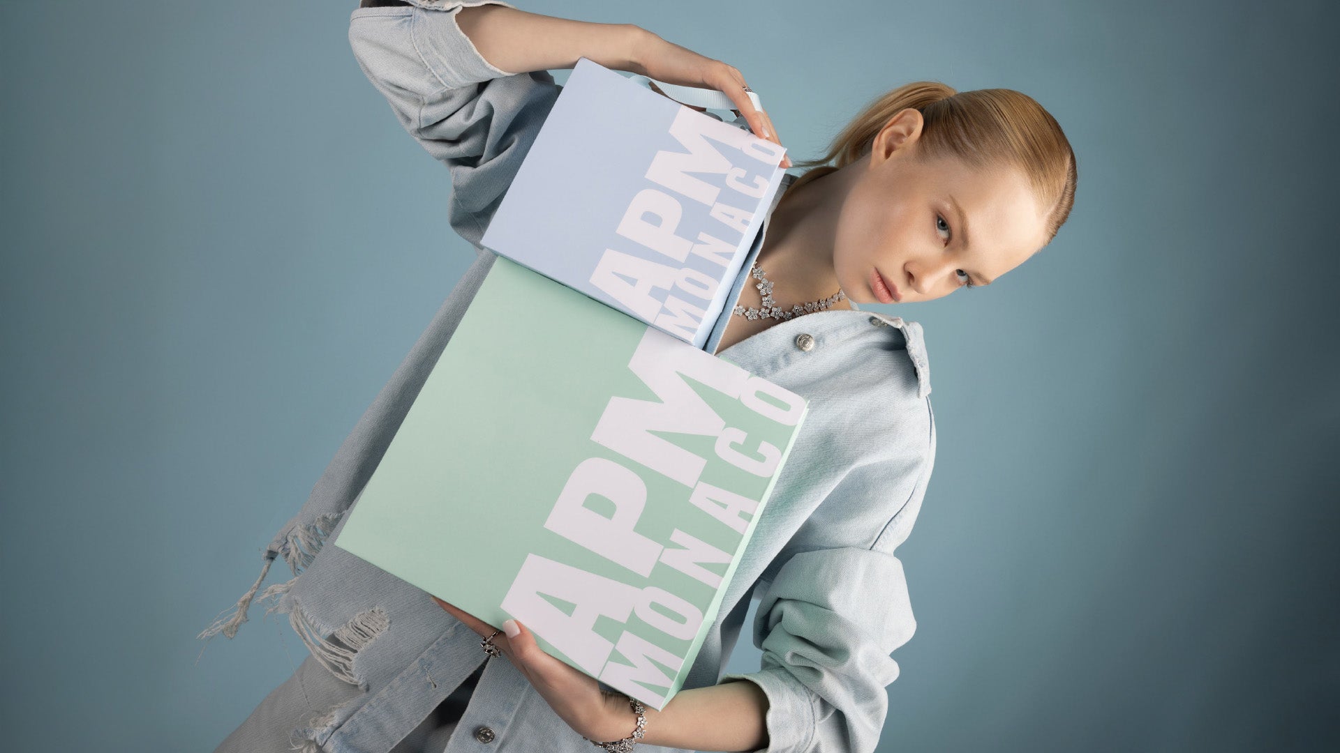 Person holding two APM Monaco gift boxes against a gray background