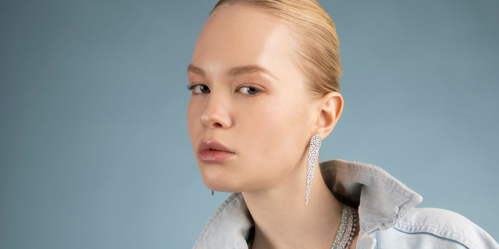 Woman wearing sparkling drop earrings against a plain background