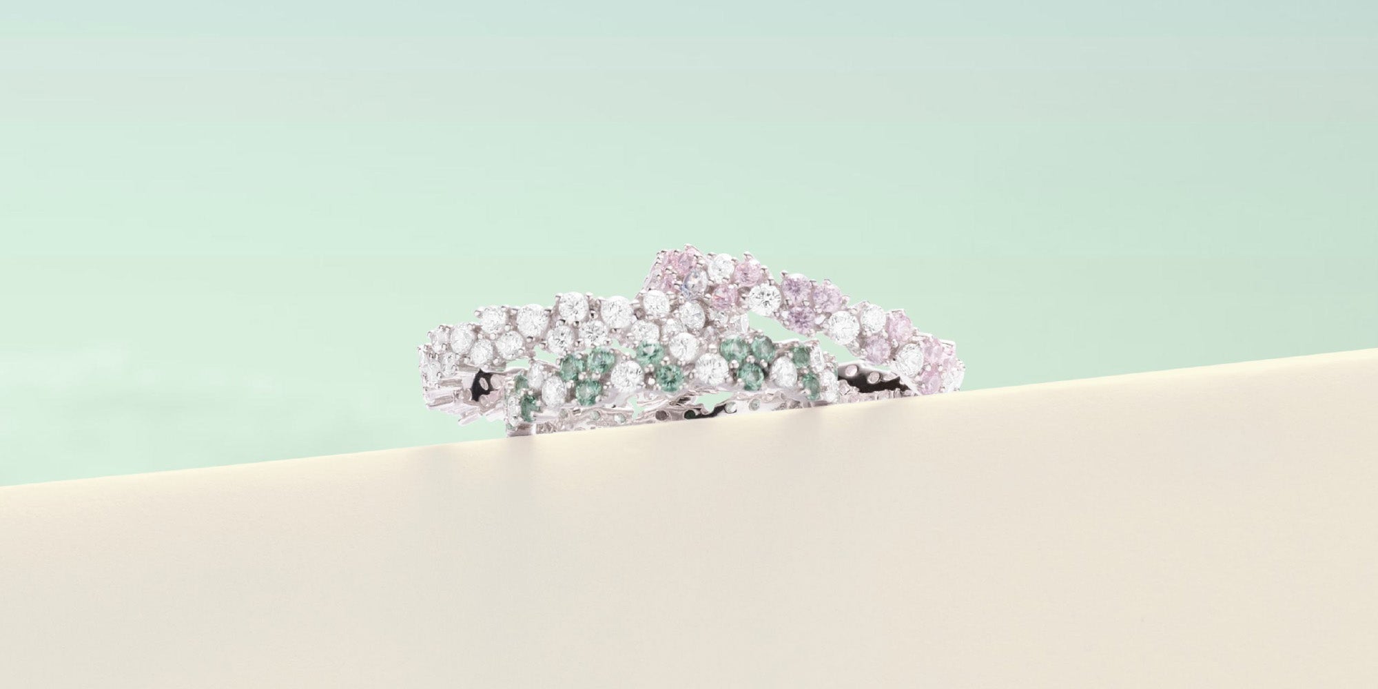 Pave rings with pastel green stones on a beige surface with a light green background